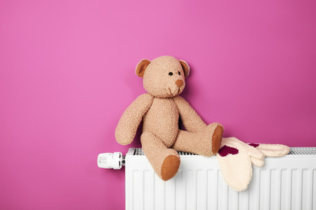 Teddy bear with mittens on heating radiator near pink wallの写真素材