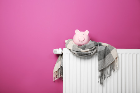 Piggy bank and scarf on heating radiator on pink backgroundの写真素材
