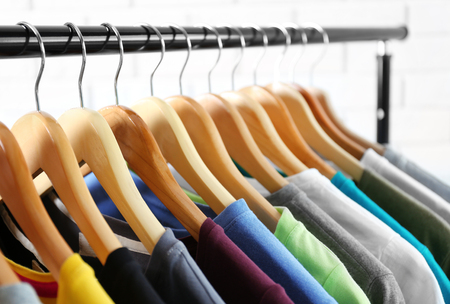 Colorful t-shirts on hangers against light blurred background, close up viewの写真素材