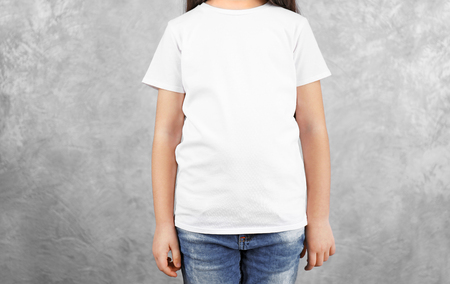 Little girl in blank white t-shirt standing against grey textured wall, close upの写真素材