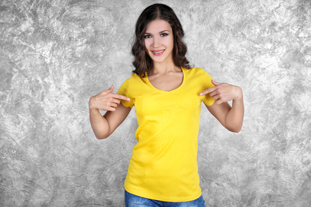 Young woman in blank yellow t-shirt standing against grey textured wallの写真素材
