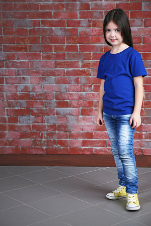 Little girl in blank blue t-shirt standing against brick wallの写真素材