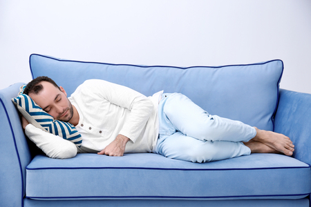 Tired barefoot man sleeping on sofa in roomの写真素材