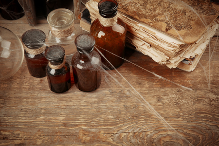 Vintage glass bottles and old books with spiderweb on wooden background, closeupの写真素材