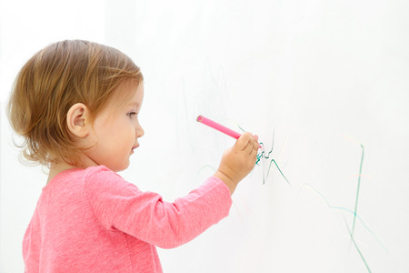 Cute little girl drawing on light wallの写真素材