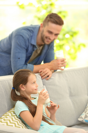 Father and daughter with glasses of fresh milk at living roomの写真素材
