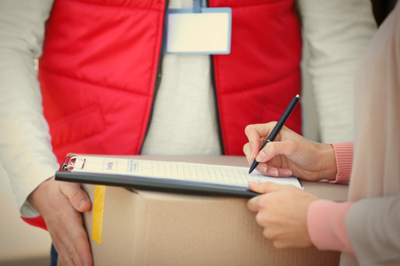 Young woman signing receipt for delivering parcel from male courier, closeup