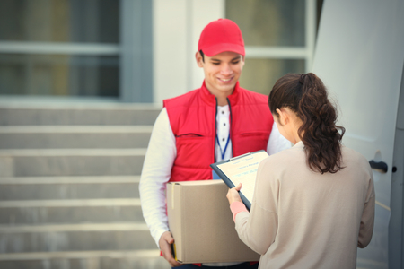 Young woman signing receipt for delivering parcel from male courierの写真素材