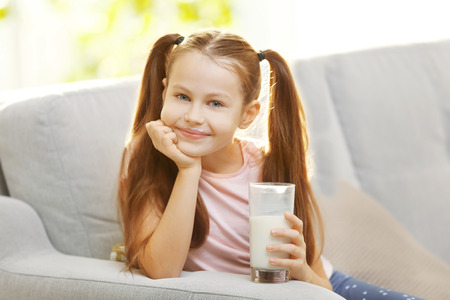 Cute little girl with glass of fresh milk on couchの写真素材