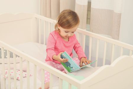 Cute little girl with book in cradle at baby roomの写真素材