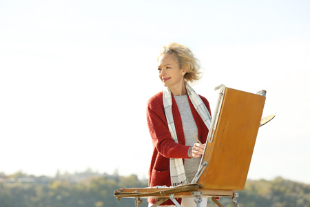 Senior female artist painting picture outdoorsの写真素材