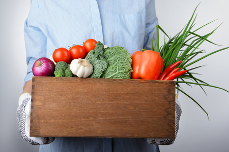 Woman holding fresh vegetables in wooden crateの写真素材