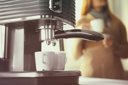 Closeup of making aromatic espresso in coffee machine and woman on backgroundの写真素材