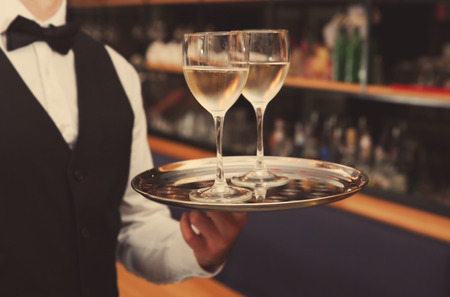 Young handsome waiter holding tray with wine glasses in the restaurantの写真素材