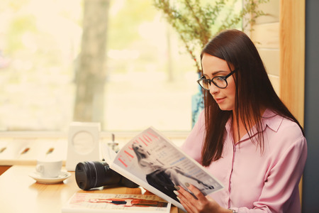 Beautiful young photographer reading magazine in cafe