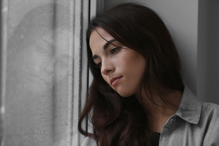Depressed young woman near window at home, closeup