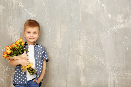 Cute boy with bouquet of beautiful flowers near grunge wallの写真素材