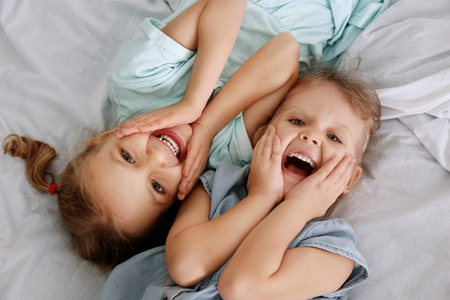 Adorable little sisters lying in bed, top view
