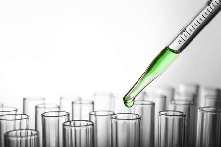 Closeup of a pipette dropping green sample into a test tube on grey backgroundの写真素材