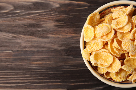 Bowl with cornflakes on wooden background
