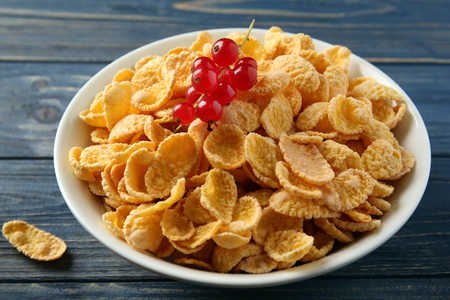 Bowl with cornflakes and red currant on grey wooden background