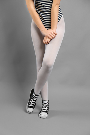 Woman in white tights and sneakers on gray backgroundの写真素材