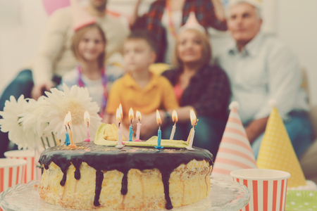 Birthday cake with alight candles and big family on backgroundの写真素材