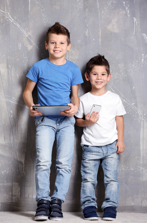 Cute little brothers using gadgets on grey textured backgroundの写真素材