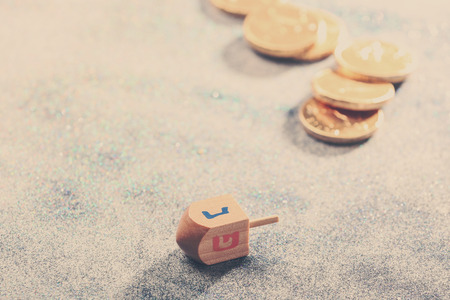 Wooden dreidel for Hanukkah on light sparkling background