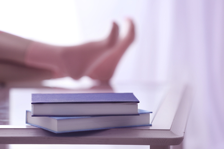 Books on glass table, on blurred human legs in knitted socks backgroundの写真素材