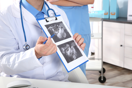 Doctor showing baby ultrasound image to pregnant woman