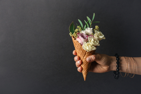 Female hand holding waffle cone with composition of flowers and branches on dark backgroundの写真素材