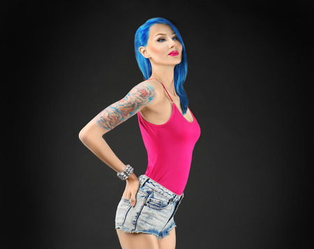 Beautiful young woman with stylish color hair and tattoo on dark backgroundの写真素材