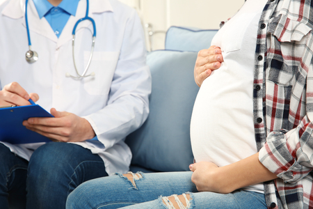 Doctor filling medical record of pregnant womanの写真素材