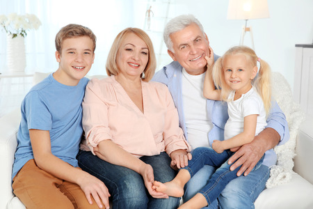 Cute happy children with grandparents sitting on sofa in living room