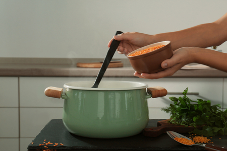 Female hand holding ladle and bowl lentil above enamelled pan in kitchenの写真素材