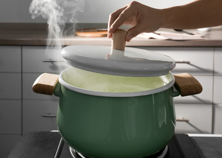 Female hand holding lid above pan in kitchenの写真素材