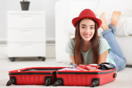 Beautiful young woman packing suitcase at homeの写真素材