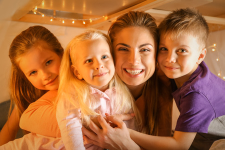 Young woman and cute children playing in hovel at homeの写真素材