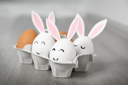 Easter eggs with paper ears in carton box on tableの写真素材