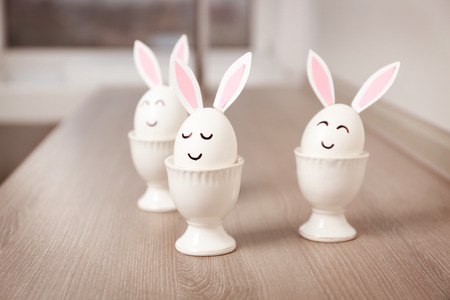 Easter eggs with paper ears in cups on table