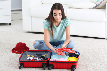 Beautiful young woman packing suitcase at homeの写真素材
