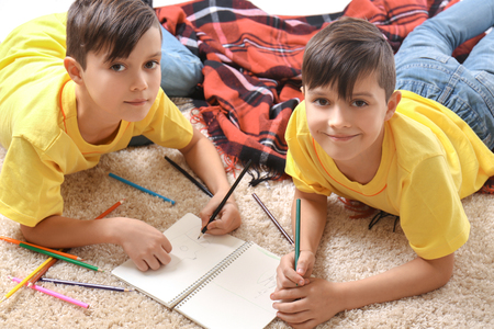 Twin brothers drawing in notebook on floorの写真素材