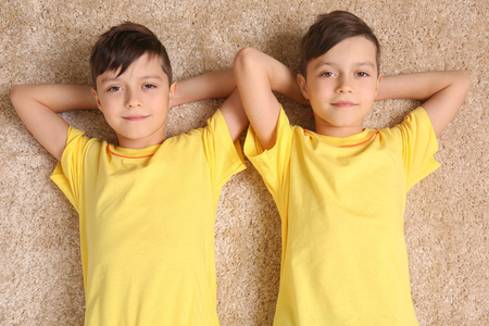 Twin brothers lying on carpetの写真素材