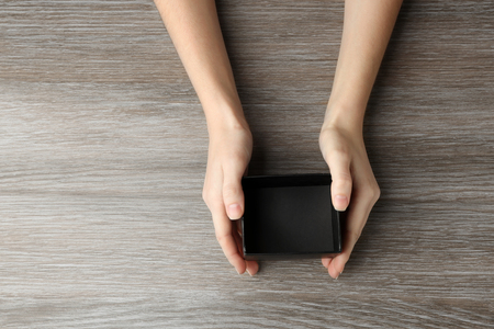 Female hands with black open box on wooden background