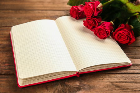 Beautiful red roses with notebook  on wooden backgroundの写真素材