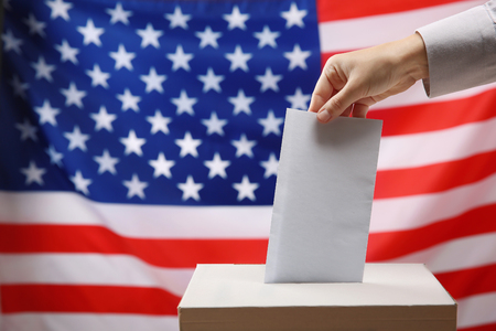 Hand inserting envelope in ballot box on USA national flag backgroundの写真素材