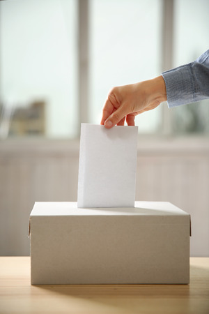 Closeup of hand inserting envelope in ballot box