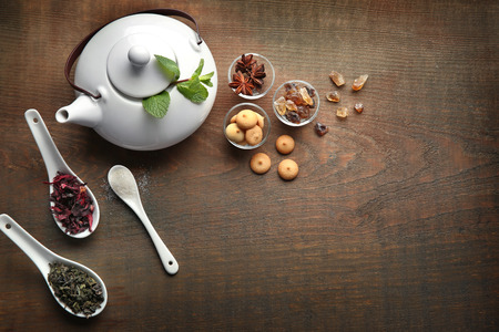 Teapot, sweets and spoons with tea on wooden tableの写真素材