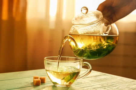 Hand pouring tea from glass teapot into a cupの写真素材